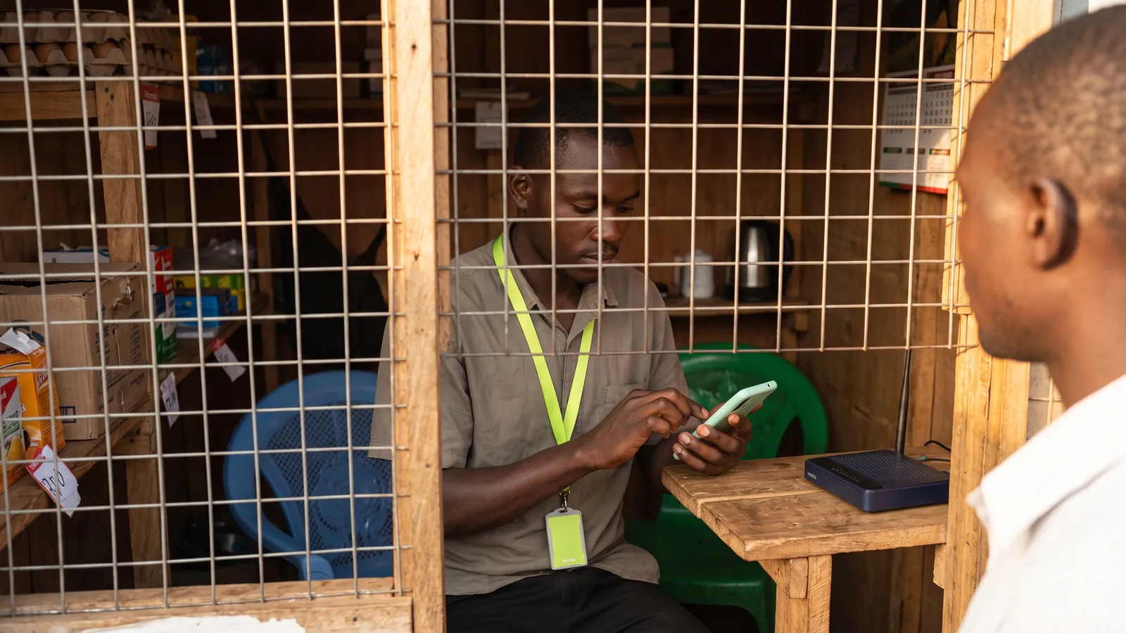 A mobile-money kiosk owner in Mbale ringing up a cash sale on a phone while the router beside him sits dark