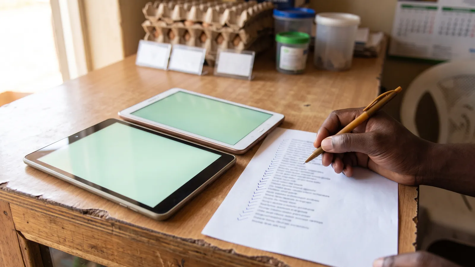 A shop owner comparing two tablets on the counter, a printed checklist beside them