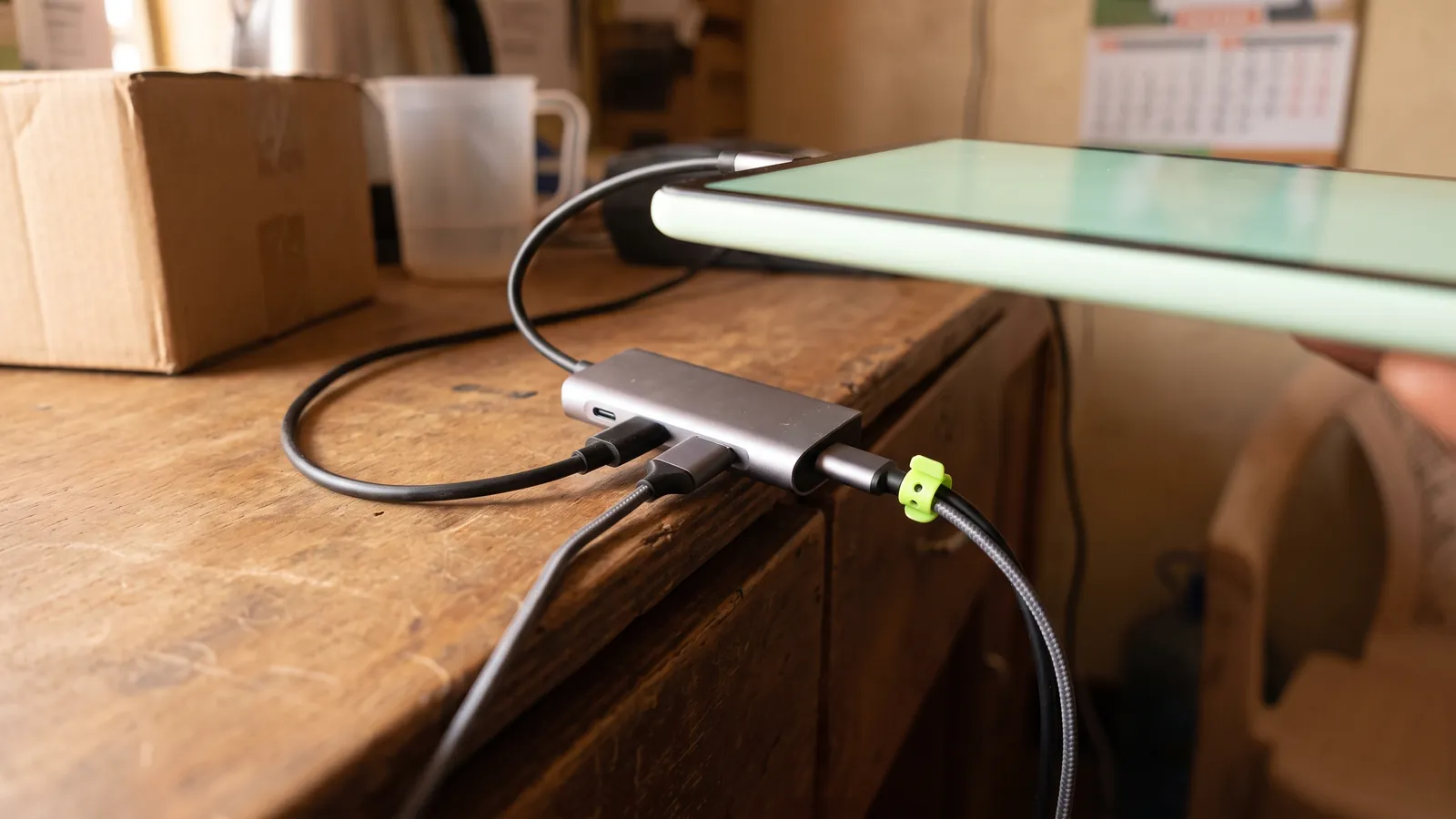 A USB-C hub on a shop counter with a printer cable and a charging cable both connected to a tablet